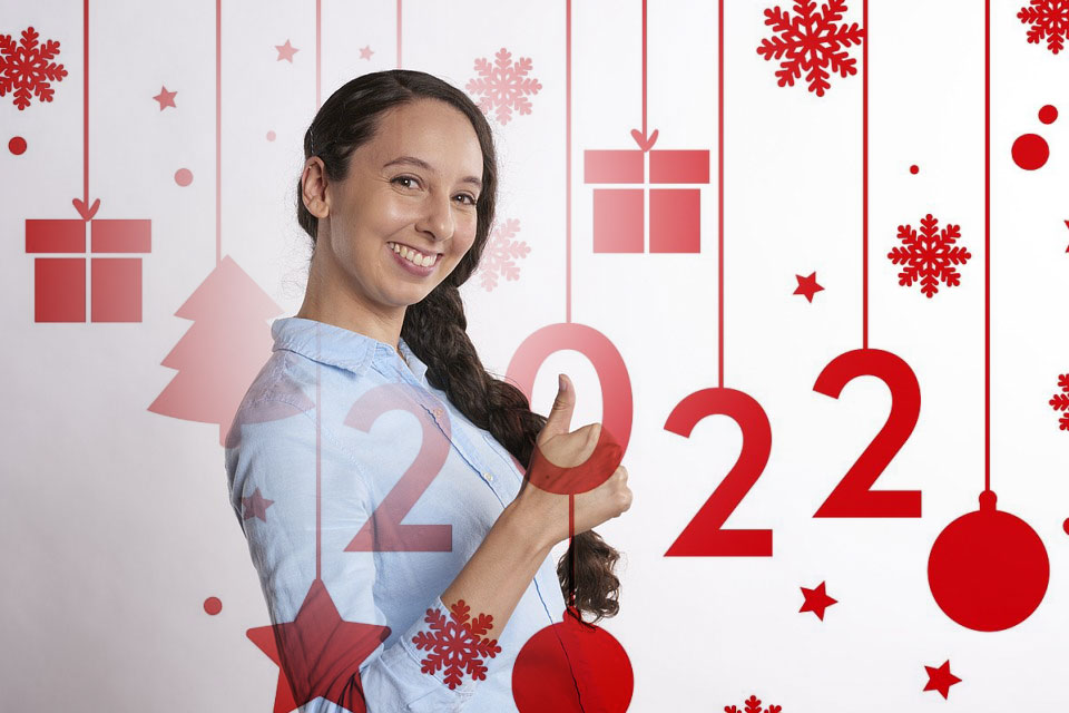 Young girl smiling at camera with long dark hair, wearing light blue shirt, posed against white background with red and pink holiday decorations including snowflakes, gift boxes, stars, ornaments, and large "22" numerals.