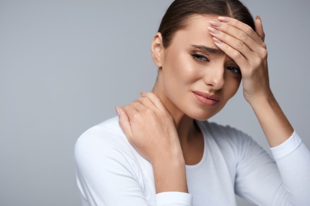 Woman experiencing head and neck pain, touching forehead and shoulder area