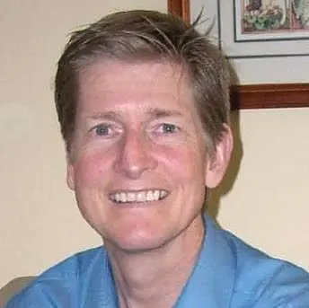 Dr. Gregory Lind smiling, with short brown hair and a blue shirt, in his office