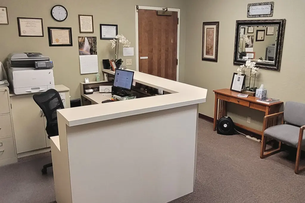 The front desk and waiting chairs, with framed certificates and a wall clock on sage-green walls