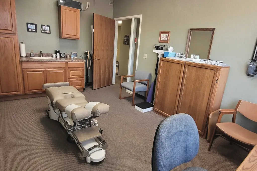 An exam room with an adjusting table, wooden cabinets, a sink and a whiteboard