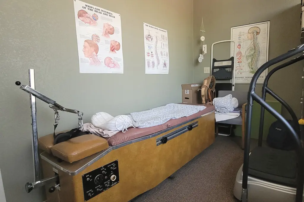 A roller traction table and a vibration platform under anatomy posters of the spine and nerves